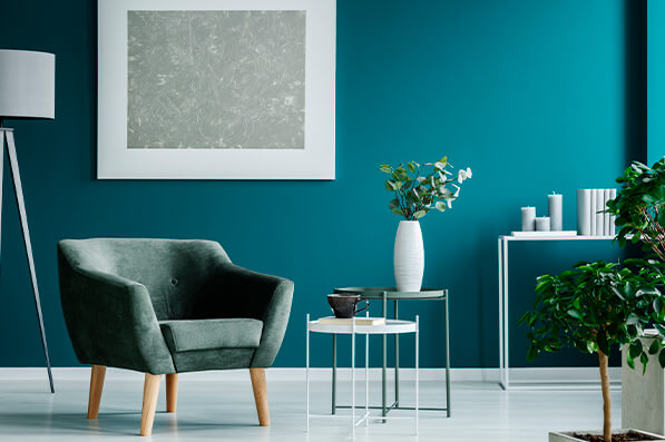 Turquoise accent wall in living area with blue/green armchair and white decorative pieces and floor